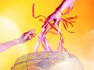 zwei Arme berühren Papierstreifen, die von Ventilator zum Fliegen gebracht werden