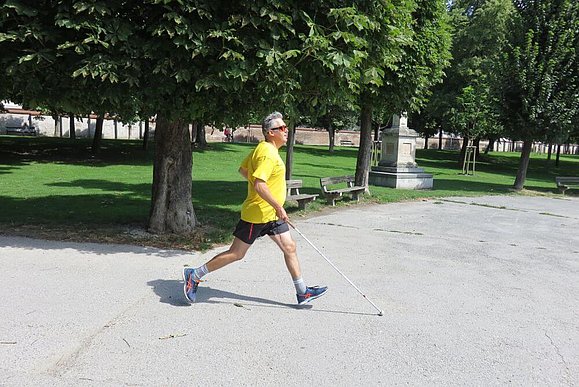 Laufender Mann mit gelbem T-Shirt und weißem Stock in der Hand