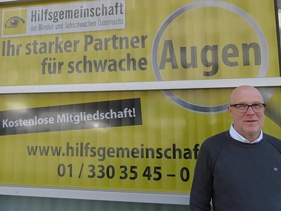 Mitarbeiter Daniele M. steht vor einem gelbschwarzen Plakat der Hilfsgemeinschaft