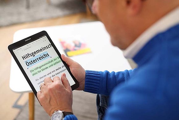 Blick über Schulter eines Mannes, der ein Zablet verwendet. Die angezeigte Website ist sehr nah herangezoomt und der Text ist teilweise farblich markiert. 