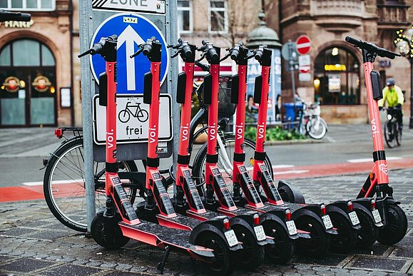 mehrere rote E-Scooter mit Aufschrift "VOI" ordentlich nebeneinandergeparkt