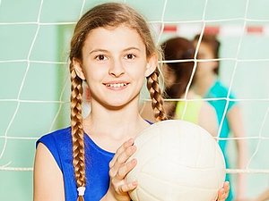 Ein Teenager-Mädchen in blauem, ärmellosen Shirt und mit Zöpfen, hält einen Volleyball in die Höhe.