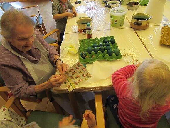 Seniorin und Kleinkind kleben Ostersticker auf grün gefärbte Eier.