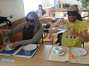 Eine Frau und ein Mann mit Augenbinden versuchen Glas und Tasse mit Wasser zu füllen