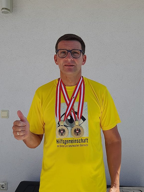 Mann mit gelbem Shirt mit Hilfsgemeinschaft Logo und zwei Goldmedaillen