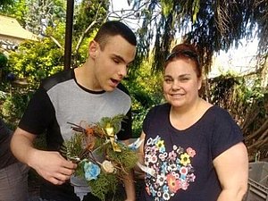 Junger Erwachsener mit Blumenkranz in Hand und Mutter