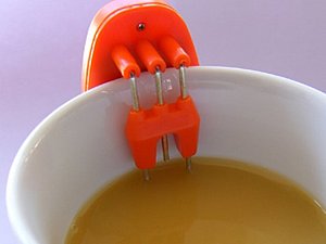 Tasse mit Kaffe und rotem Gerät geklammert an den Tassenrand, reicht bis in die Flüssigkeit hinein.