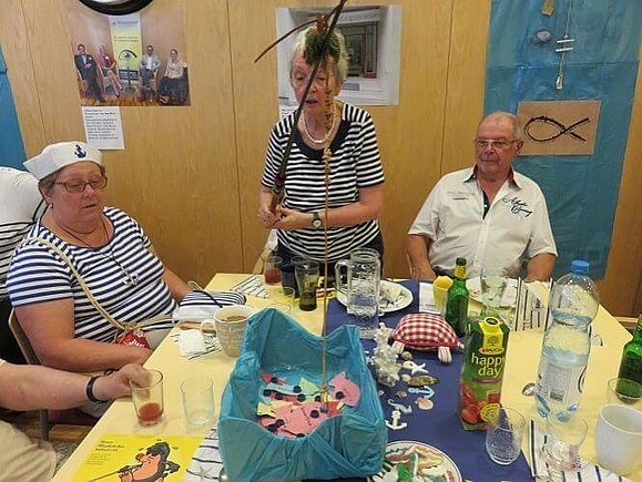 Spiele, Spaß und Spannung 3 Personen sitzen bei Tisch und eine Person angelt Papierfische aus der Tischmitte