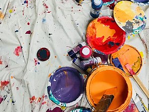 weißes Laken am Boden mit offenen bunten Farbtöpfen und Pinseln