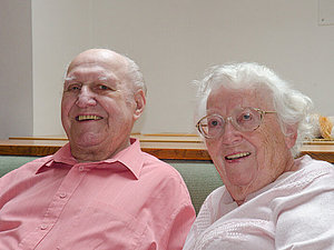 Ein älteres Ehepaar sitzt einander zugeneigt lachend nebeneinander