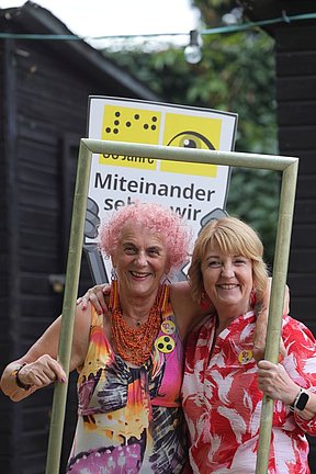 Es war ein unglaublich gelungenes Fest Zwei Frauen halten einen Bilderrahmen, hinter ihnen die Pappfigur vom Maskottchen AUGust