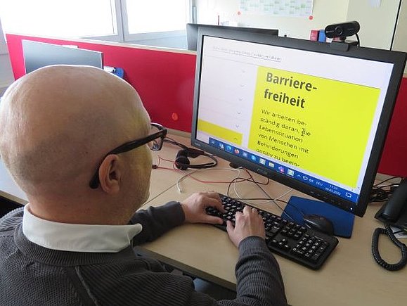 Mitarbeiter Daniele M. sitzt vor seinem Computer, eine Vergrößerungssoftware hilft ihm beim Lesen des Bildschirms.
