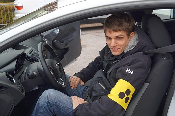 Ein blinder junger Mann sitzt in einem Auto auf dem Fahrersitz