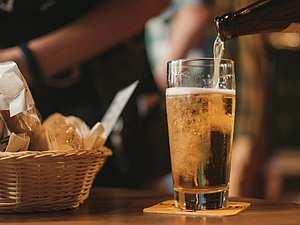 Helles Bier im Glas wird eingeschenkt mit Brotkorb auf einem Tisch