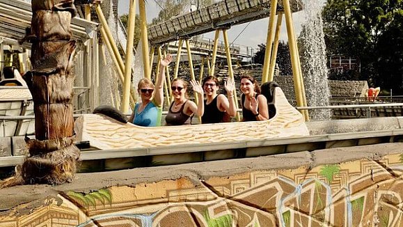 Vier Mitarbeiterinnen sitzen in einem ausgehöhlten Baumstamm der Wasserbahn.