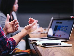 Meetingsituation: gestikulierende Hände und Laptop am Tisch mit Handy
