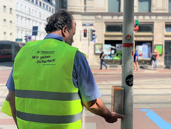 Mann mit gelber Warnweste von hinten drückt Akustikampel