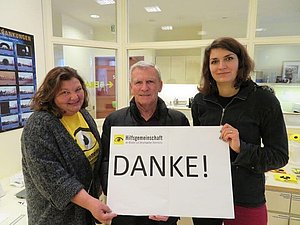 Zwei Frauen und ein Mann halten lächelnd ein Danke-Schild in die Kamera