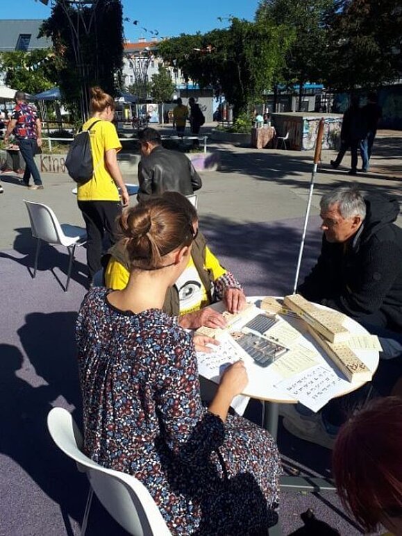 3 Personen sitzen bei einem Tisch und testen die Brailleschrift