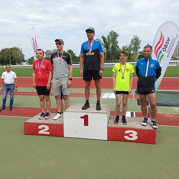 Mehrere Männer in Sportkleidung stehen auf Gewinnerpodest 1, 2 und 3