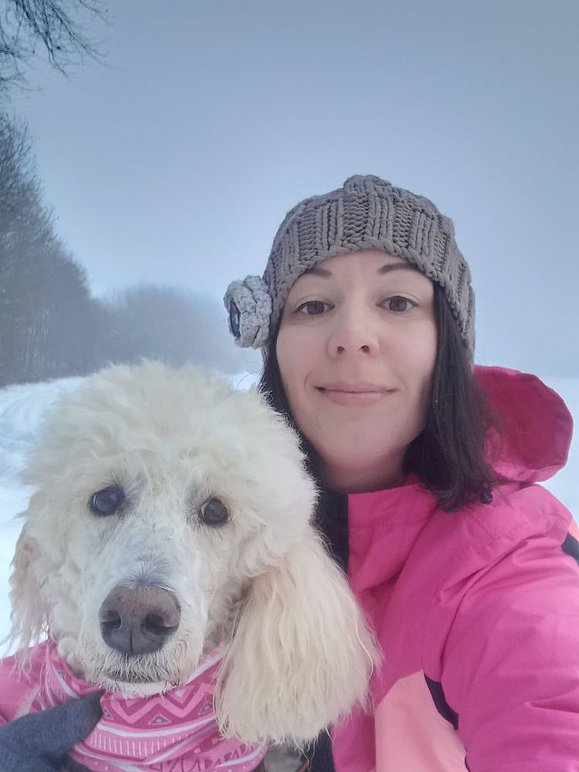 Junge Frau mit pinker Jacke und weiße Hündin vor Schneelandschaft