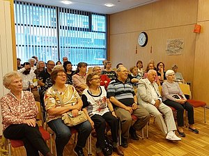 Gruppe von Personen sitzen auf Stühle in Veranstaltungsraum und achten auf die Präsentation vor ihnen