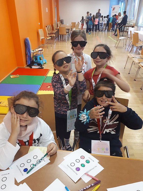 mehrere Kinder mit schwarzen Übungsbrillen posieren für die Kamera