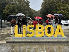 Man sieht große Buchstaben mit "LISBOA" auf einem Platz, dahinter stehen Personen