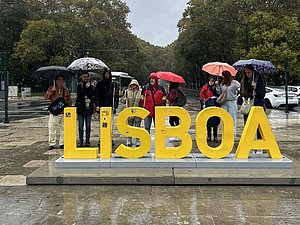 Man sieht große Buchstaben mit "LISBOA" auf einem Platz, dahinter stehen Personen