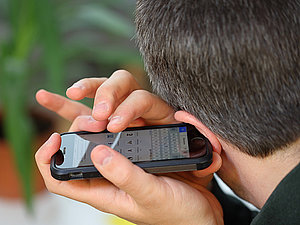 Mann hält sich ein Handy ans Ohr und bedient den Touchscreen dabei mit den Fingern. 