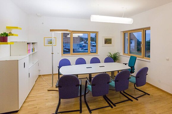 Ein Besprechungsraum der mit einer Stehleuchte und einer rohrförmigen Deckenleuchte beleuchtet wird