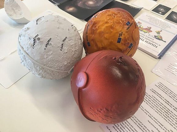 Drei bunte 3D-Planeten mit taktilen Elementen leigen zusammen auf einem Tisch.
